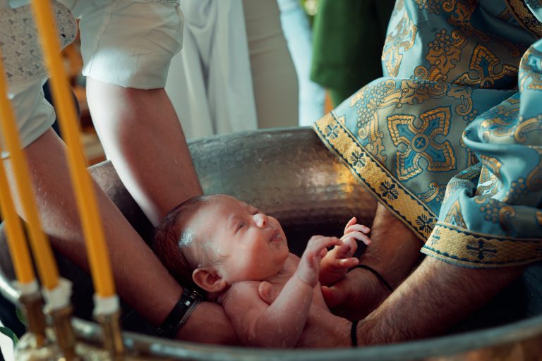 Nașul o ține cu grijă pe micuța Aria în brațe, la botezul din Paris