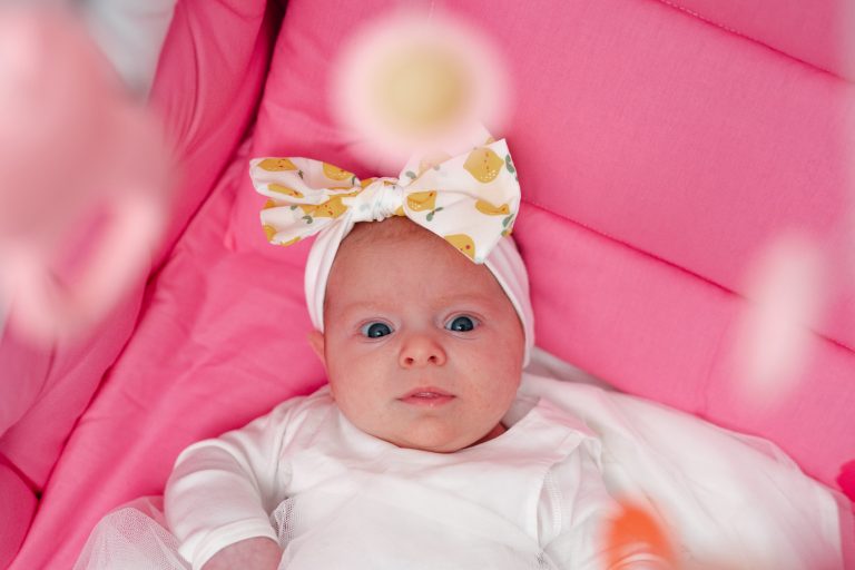 Olivia întinsă pe spate în pătuțul roz, privind curioasă spre cameră