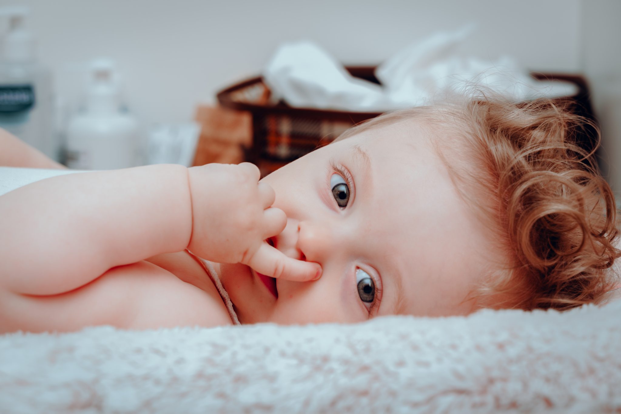 Carolina întinsă în pătuț, cu mâna la gură, privind spre cameră